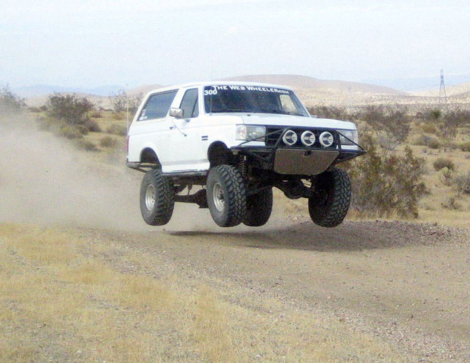 White lifted Ford Bronco catching air on a dirt desert road