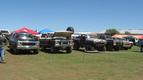 1978 Ford Bronco - Several trucks and SUVs are parked on a grassy field under a clear blue sky.