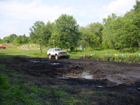 1992 Ford Bronco - A white SUV navigates a muddy track during an off-road event.