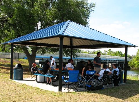 2006 Mazda 6 - A group of people are socializing under a covered picnic area on a sunny day.