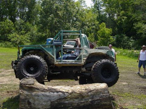 1992 Ford Bronco - A heavily modified off-road vehicle navigates a log obstacle during an event.
