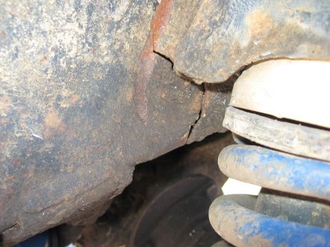 1974 Ford F-100 - The underside of a vehicle shows significant rust and a crack in the frame, with a blue coil spring visible.