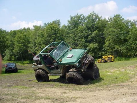 1992 Ford Bronco - An off-road vehicle is shown tilted on its side in a grassy field with trees in the background.