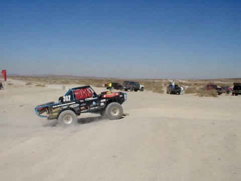 1996 Ford Bronco - A modified truck races across a dusty desert landscape with other vehicles in the background.