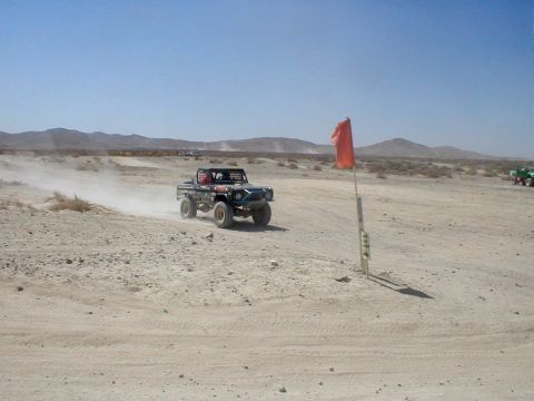 1996 Ford Bronco - Off-road truck racing on a dusty desert course with mountains in the background.