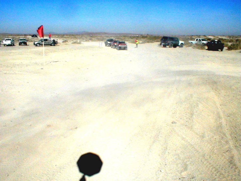 Several off-road vehicles parked in a sandy, open area under a clear blue sky