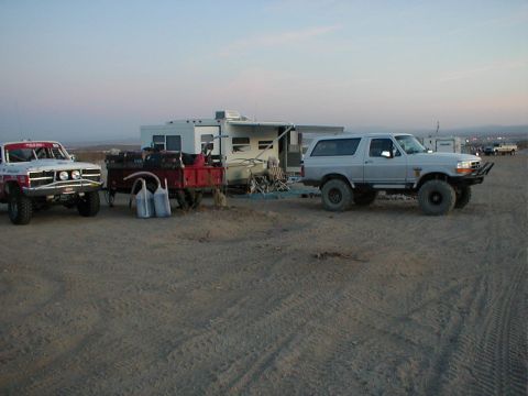 1996 Ford Bronco - A silver Ford Bronco is parked on a dirt lot next to a trailer and another vehicle.