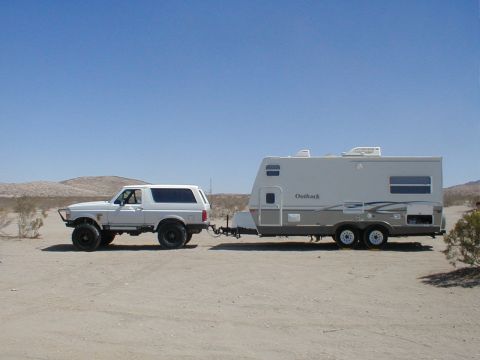 1996 Ford Bronco - A 1996 Ford Bronco tows an Outback travel trailer across a dry, open area under a clear blue sky.