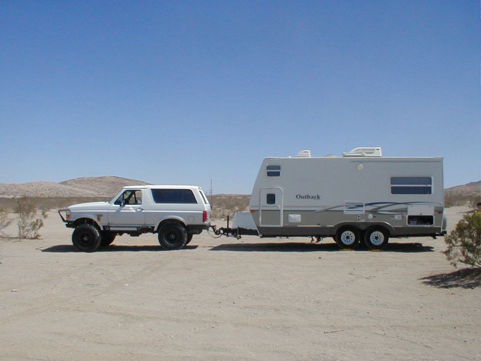 1996 Ford Bronco towing an Outback travel trailer in a desert landscape