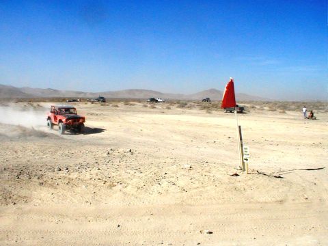 1996 Ford Bronco - An off-road vehicle races across a dusty desert landscape under a clear blue sky.
