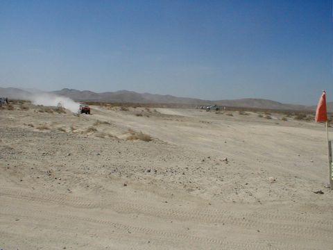 1996 Ford Bronco - Several vehicles traverse a dusty desert terrain under a clear blue sky, with an orange flag marking the course.