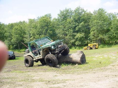 1992 Ford Bronco - Off-road vehicle navigates a large log obstacle during an event, with another vehicle visible in the distance.