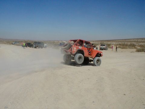 1996 Ford Bronco - An orange 1996 Ford Bronco is captured mid-air during an off-road event, kicking up dust.