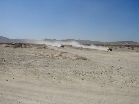 1996 Ford Bronco - Several vehicles traverse a dry, dusty terrain under a clear blue sky, with mountains in the distance.