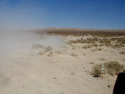 1996 Ford Bronco - A vehicle kicks up a large dust cloud while traversing a dry, desert terrain under a clear blue sky.