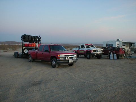 1996 Ford Bronco - Two trucks, a trailer, and a camper are staged in a desert landscape under a clear sky.
