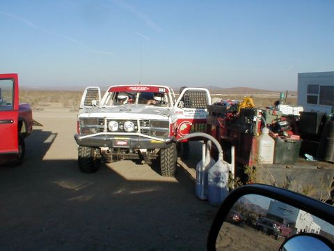1996 Ford Bronco - A desert scene shows an off-road race truck with safety modifications, parked beside another vehicle and equipment.