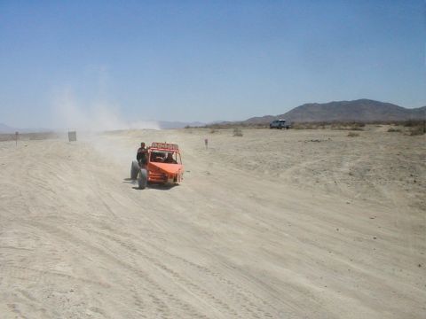 1996 Ford Bronco - An orange dune buggy navigates a dusty desert track with a second vehicle visible in the distance.