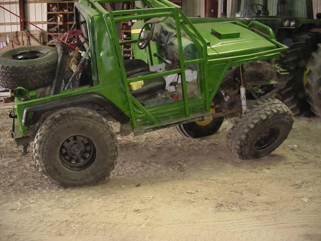Green off-road vehicle with roll cage, spare tire mounted on rear, and large tires