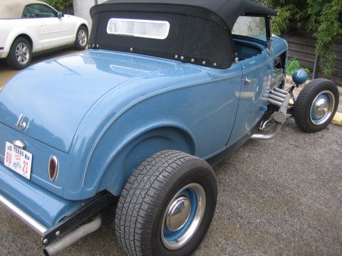 1996 Ford Bronco - A blue hot rod roadster is parked next to a white convertible. The hot rod has a black soft top and exposed exhaust pipes.