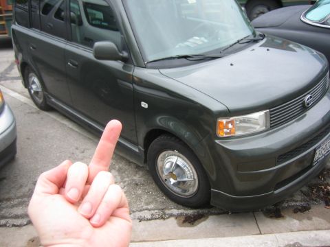 1996 Ford Bronco - A hand gives the middle finger in front of a dark green SUV parked on the street.