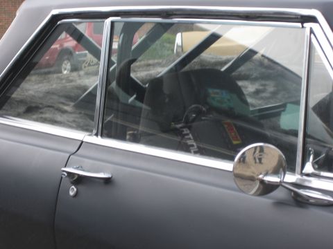 1996 Ford Bronco - Interior view of a car with a roll cage, showing a racing seat and a reflection of a red truck in the window.