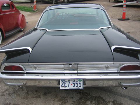 1996 Ford Bronco - Rear view of a black classic car distinctive tail fins and a chrome bumper. A red vintage car is partially visible to the left.