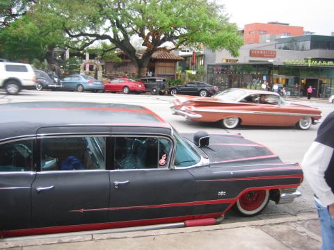 1996 Ford Bronco - A customized sedan with red accents is parked curbside, with other vehicles and businesses visible.