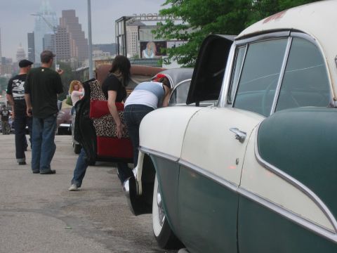 1996 Ford Bronco - People gather around a classic car with its hood open, with a city skyline in the background.