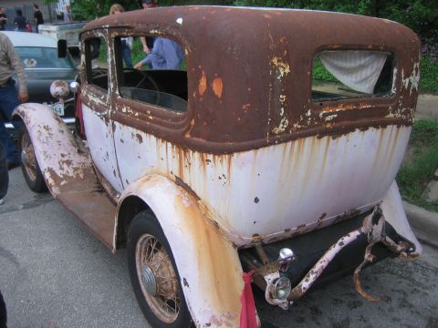 1996 Ford Bronco - This heavily rusted vintage sedan is seen from the rear, with another vehicle in the background.