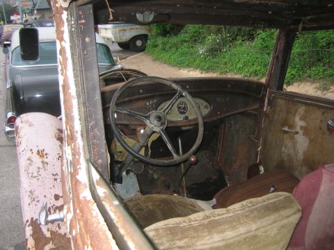 1996 Ford Bronco - The interior of a dilapidated vintage automobile shows significant rust and wear, with a steering wheel and dashboard instruments.