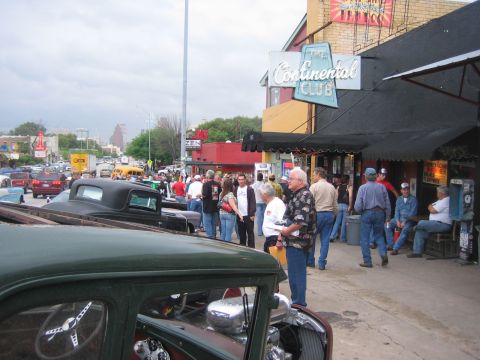 1996 Ford Bronco - A street scene with multiple classic cars and people congregating outside a club.