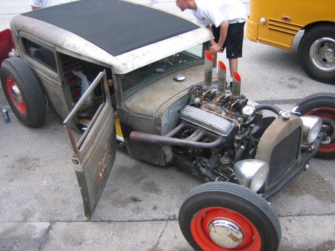 1996 Ford Bronco - A custom hot rod with a prominent V8 engine and open driver's side door sits next to a yellow bus.