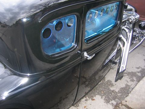 1996 Ford Bronco - A black hot rod car with distinctive blue tinted windows and prominent chrome exhaust pipes is viewed from its side.