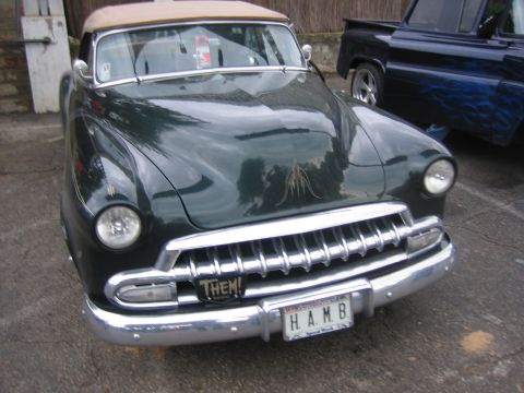 1996 Ford Bronco - A dark green convertible with a tan top is parked next to a blue pickup truck.