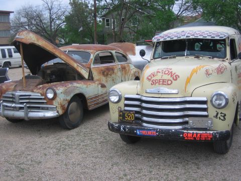 1996 Ford Bronco - Two vintage vehicles, a heavily rusted sedan and a decorated truck, are parked outdoors.