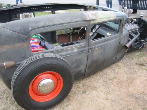 1996 Ford Bronco - A custom rat rod sedan with a weathered finish, exposed engine, and a colorful blanket visible through the open windows.