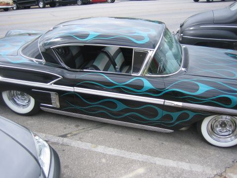 1996 Ford Bronco - A classic black 1958 Chevrolet Impala with teal flame graphics is parked next to another vehicle.