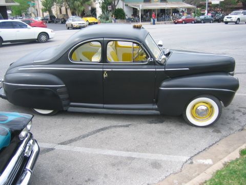 1996 Ford Bronco - Side view of a black customized coupe with a yellow interior and unique wheels parked on a street.