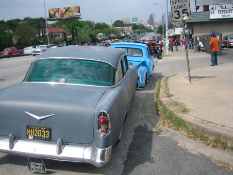 1996 Ford Bronco - A gray 1955 Chevrolet Bel Air is parked on the street next to a blue pickup truck, with a cityscape in the background.