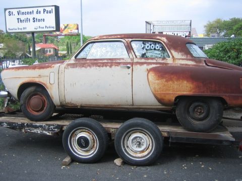 1996 Ford Bronco - A heavily rusted sedan is transported on a flatbed trailer.