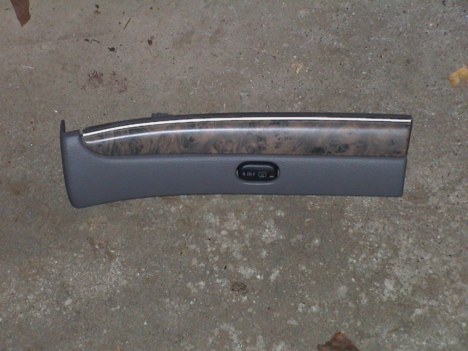 Grey dash trim panel with woodgrain insert and rear defroster switch lying on concrete