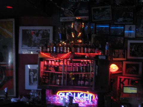 1996 Ford Bronco - A dimly lit bar scene features shelves stocked with bottles, illuminated by red and purple lights, with a neon Bud Light sign prominent.