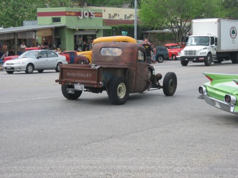 1996 Ford Bronco - A heavily modified, rusty Chevrolet pickup truck with a yellow kayak on its roof drives down a street.