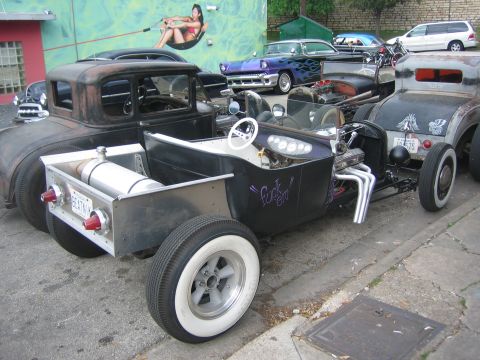 1996 Ford Bronco - A collection of modified vehicles are parked together on a street, with a mural on the building behind them.