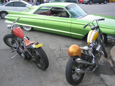1996 Ford Bronco - Two custom motorcycles are parked alongside a vintage green car, with other vehicles visible in the background.