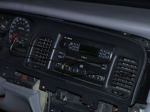 2000 Ford Crown Victoria - Ford dash bezel pulled forward from the dashboard with the factory AM/FM CD radio and center vents still mounted in it, hanging on a pair o…
