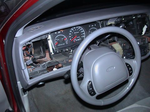 2000 Ford Crown Victoria - Driver-side view through the open door of a red Ford sedan with the grey dash pad and instrument bezel removed, exposing bare metal structu…