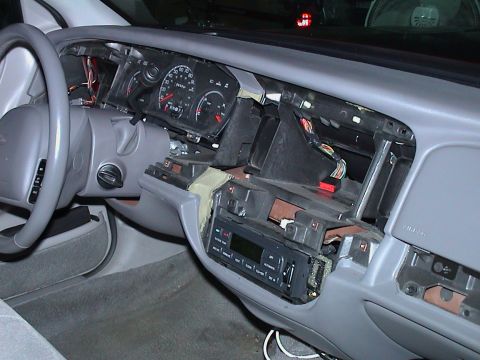 2000 Ford Crown Victoria - Gray interior of a Ford sedan with the center dash bezel removed, exposing the HVAC control head, radio cavity and wiring harnesses behind…