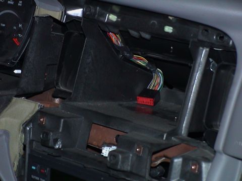 2000 Ford Crown Victoria - Detail of the empty radio bay behind a removed dash bezel, with a disconnected red multi-pin radio connector and its ribbon of colored wire…